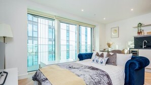 A modern bedroom with a large bed, a sofa, and a dining area with a view through large windows. - Cosy London Apartment Near River Thames (London)
