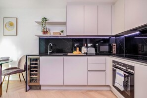 A modern kitchen with a black countertop, white cabinets, a built-in oven, and a microwave. - Cosy London Apartment Near River Thames (London)