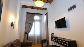 A living room with a sofa, a coffee table, a TV mounted on the wall, and a window with curtains. - KamilBey Suite Hotel (Istanbul)
