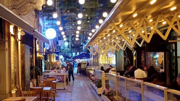 An indoor walkway with tables and chairs, overhead umbrellas, and a railing with flowers. - KamilBey Suite Hotel (Istanbul)