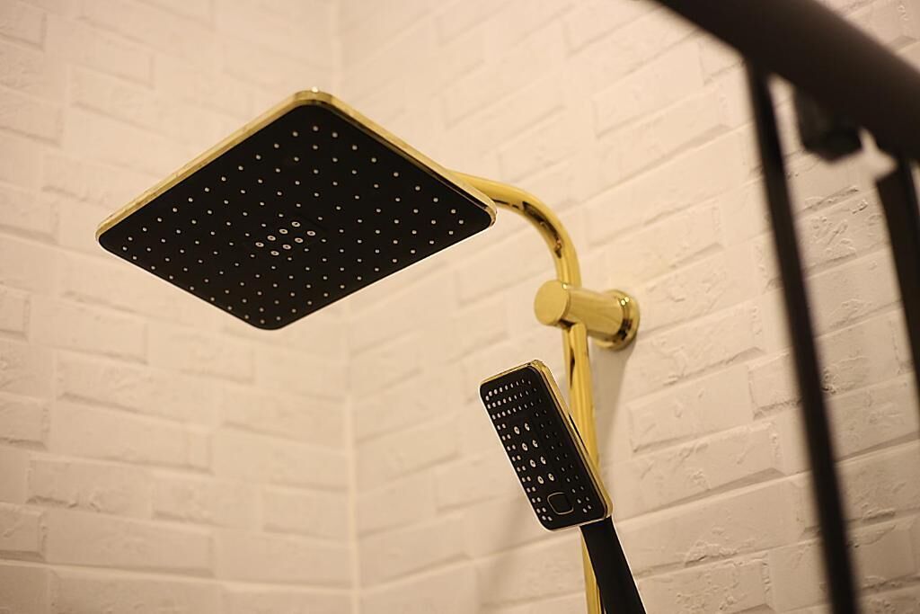 A shower with a black perforated panel and a gold-colored control panel.