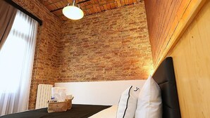 A room with a brick wall, a bed with white bedding, a wooden headboard, a hanging light fixture, and a window with curtains. - KamilBey Suite Hotel (Istanbul)