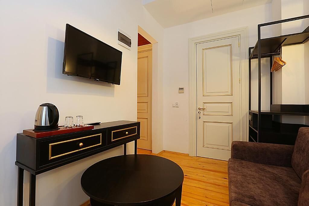 A modern living room with a flat-screen TV mounted on the wall, a black coffee table, a brown sofa, and a black TV stand with a coffee maker and glasses.