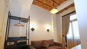 A room with a brown sofa, a black cabinet with a hanging clothes rack, two wall-mounted lights, and a large window with curtains. - KamilBey Suite Hotel (Istanbul)