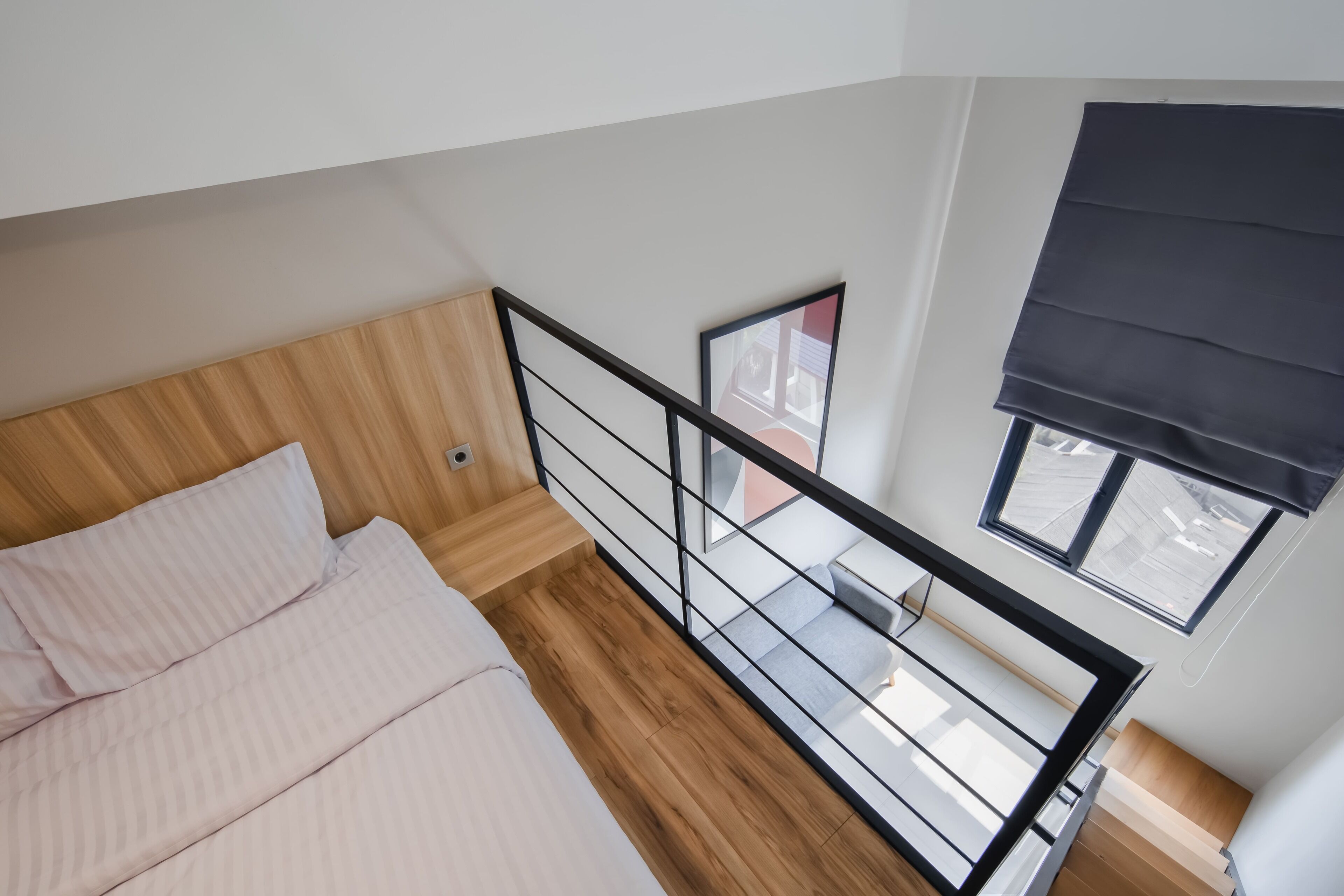 A bedroom with a wooden headboard, a bed with white bedding, a black-framed window, and a view of the outside.
