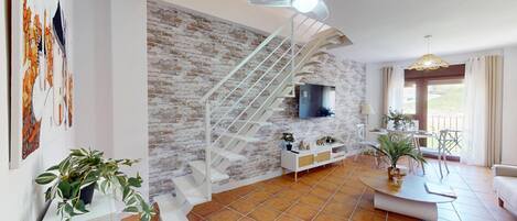 Una sala de estar con pared de ladrillo, escalera blanca, televisor de pantalla plana y plantas en macetas.