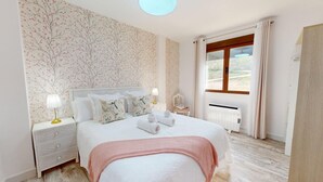 A bedroom with a bed, nightstands, a window with curtains, and a view of the outdoors.