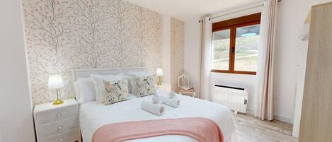 Une chambre à coucher avec un lit, des tables de chevet, une fenêtre avec des rideaux et une vue sur l’extérieur.