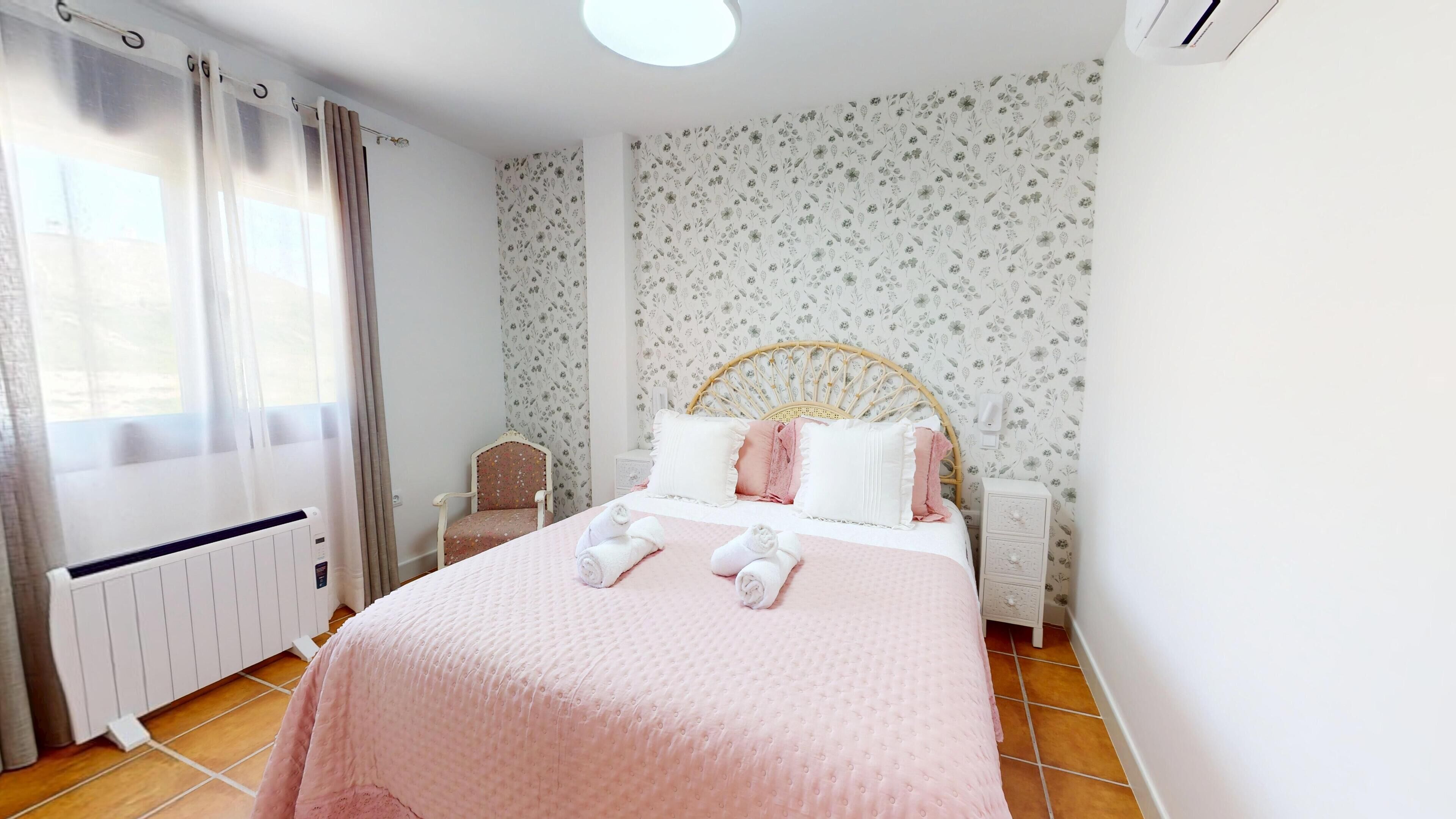 A bedroom with a bed, a chair, a radiator, and a window with curtains.