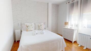 Un dormitorio ordenado con una cama grande, una mesita de noche, un aparador y una ventana con cortinas.