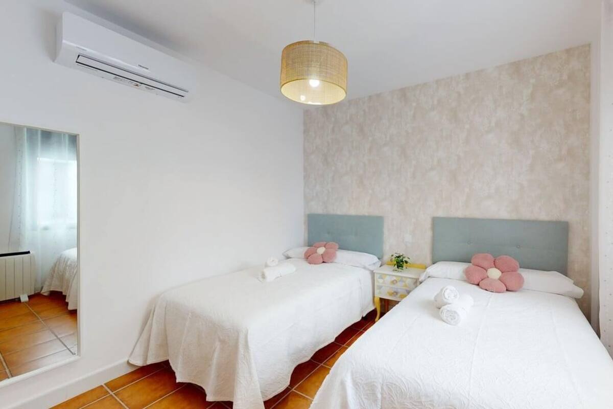 A hotel room with two beds, a mirror, a small table with a lamp, and an air conditioning unit.