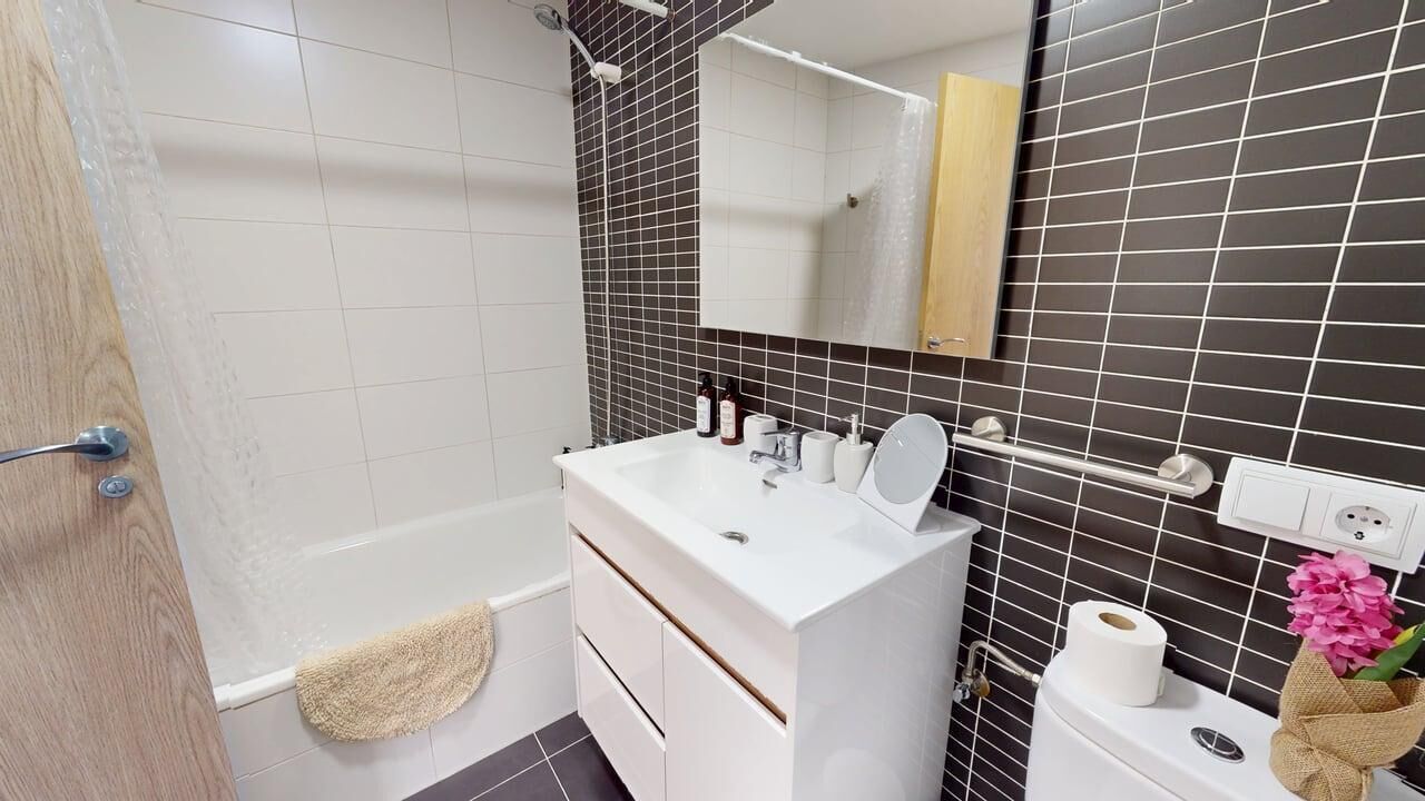 Un baño con bañera, tocador blanco con espejo y un perchero para toallas.