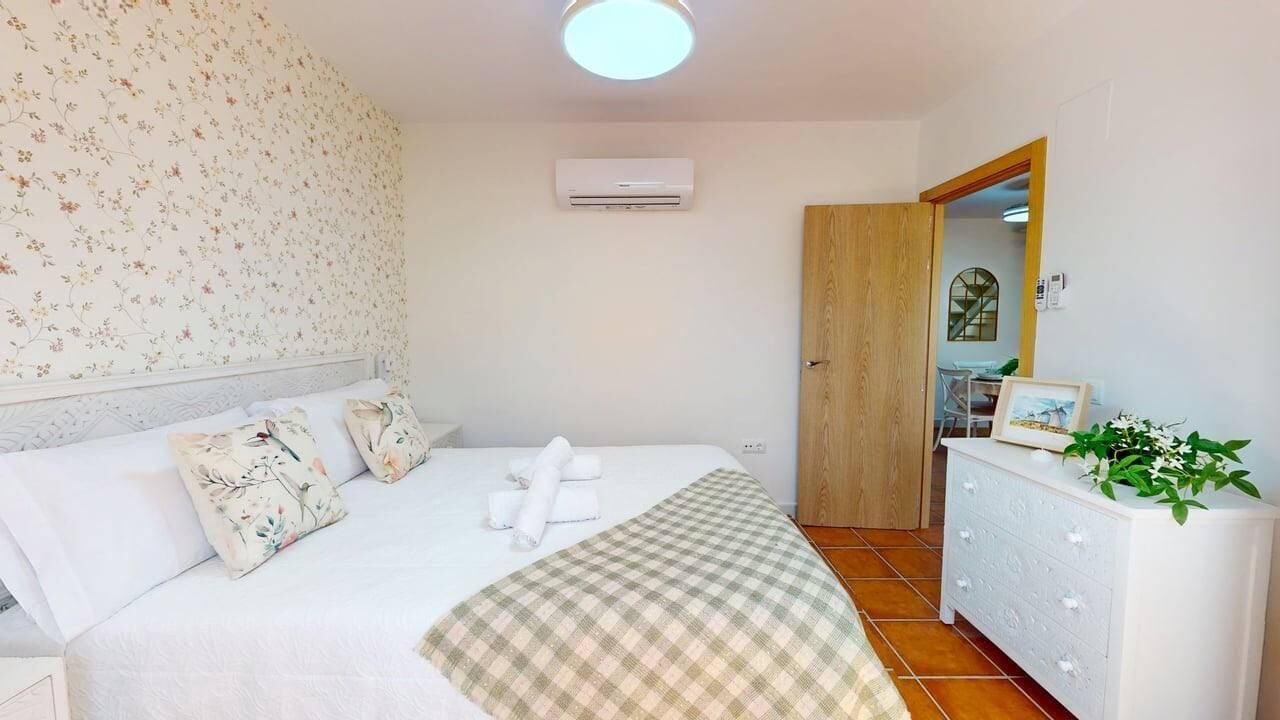 Ein Schlafzimmer mit Bett, floralem Wanddesign, Klimaanlage, Holztür, Kommode und einer Pflanze.