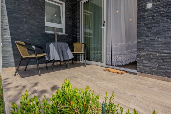 A patio with two wicker chairs, a table with a grey tablecloth, and a glass door leading to a covered area. - Apartment Mutak (Vir)