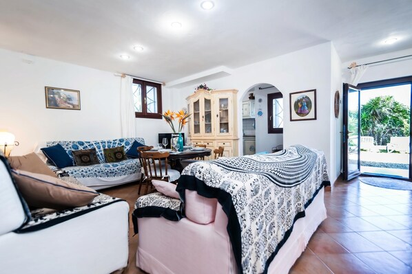 Quarto com cama, sofá, mesa de jantar e área de cozinha visível através de um arco.