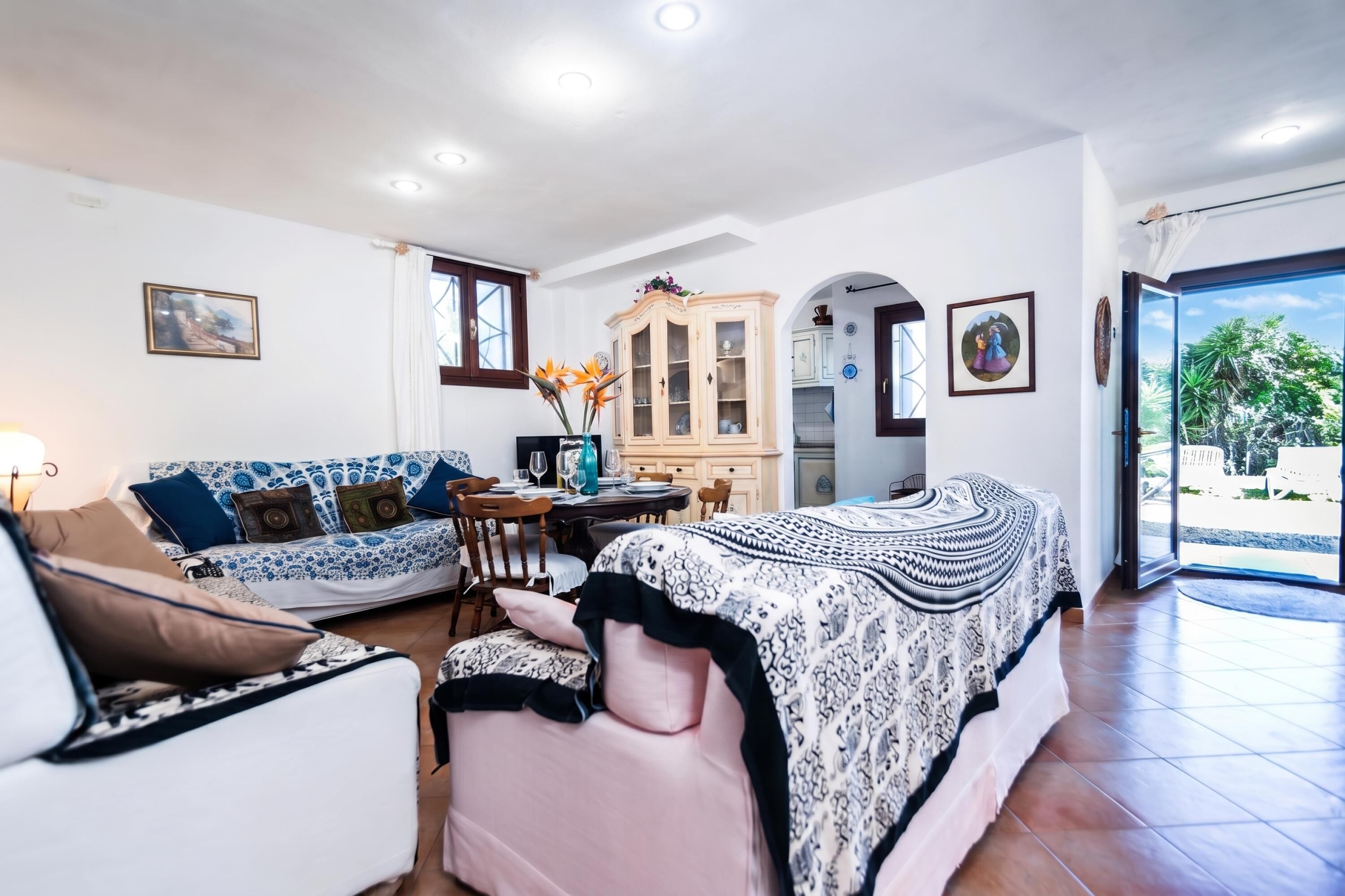 Une pièce bien éclairée, avec un canapé, une table à manger et un lit. Une fenêtre offre une vue sur la verdure à l’extérieur.