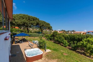 A backyard with a hot tub, outdoor furniture, and a view of a hillside with trees and houses. - La Sciumara With Beach Access (Arzachena)