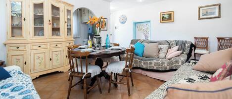 A dining area with a wooden table and chairs, a cabinet with glass doors, and a sofa with patterned cushions.