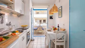 A narrow kitchen with white cabinets, a sink, and a dining area with a table set for two.