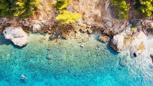 Vue aérienne d’une zone côtière caractérisée par des eaux turquoise limpides, un littoral rocheux et une végétation clairsemée.