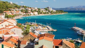 Une ville côtière dotée d’un port de plaisance, de bâtiments aux toits recouverts de tuiles rouges et d’une mer d’un bleu limpide.
