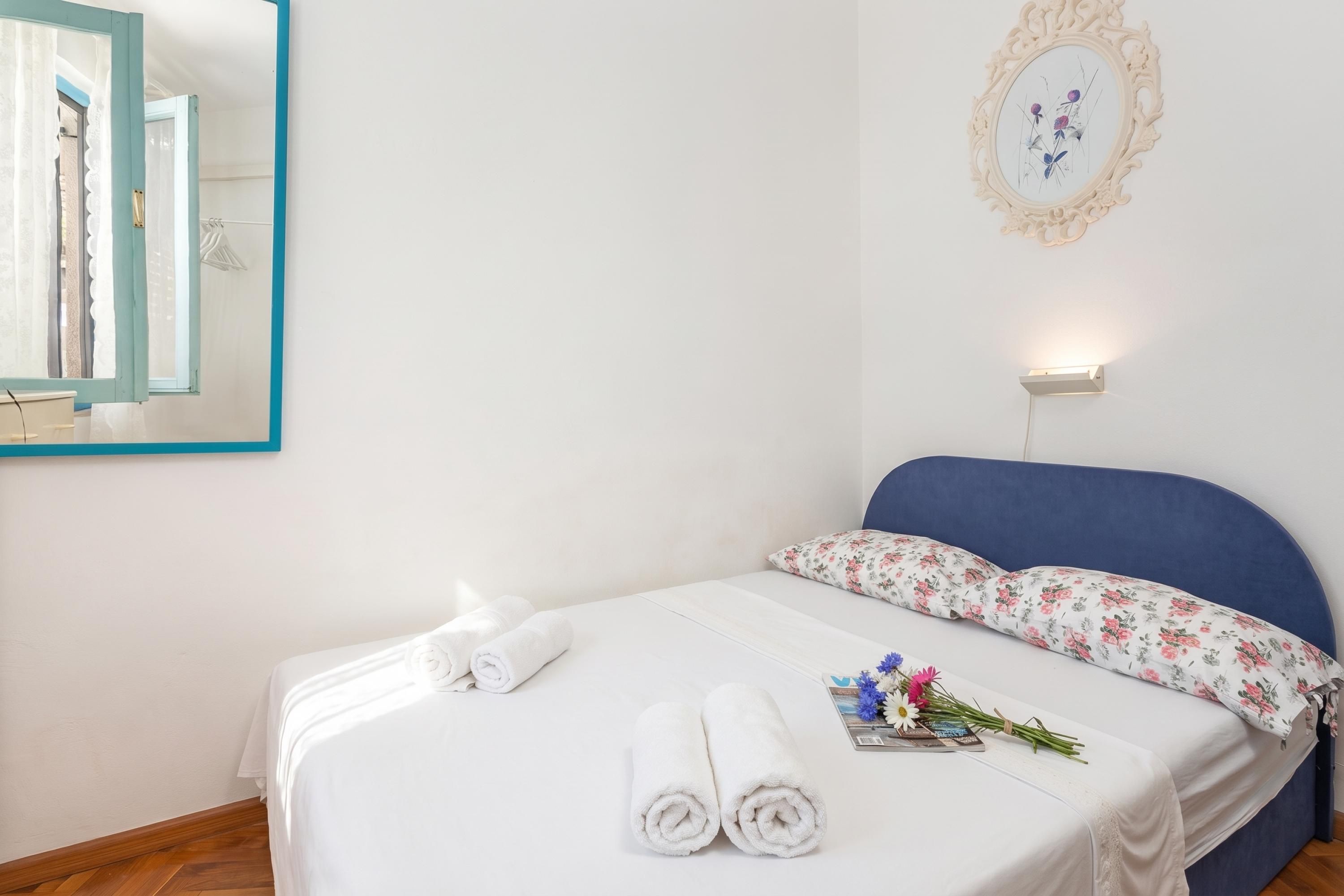 Un lit bien fait, avec des draps blancs, un coussin à motifs floraux et deux serviettes enroulées.