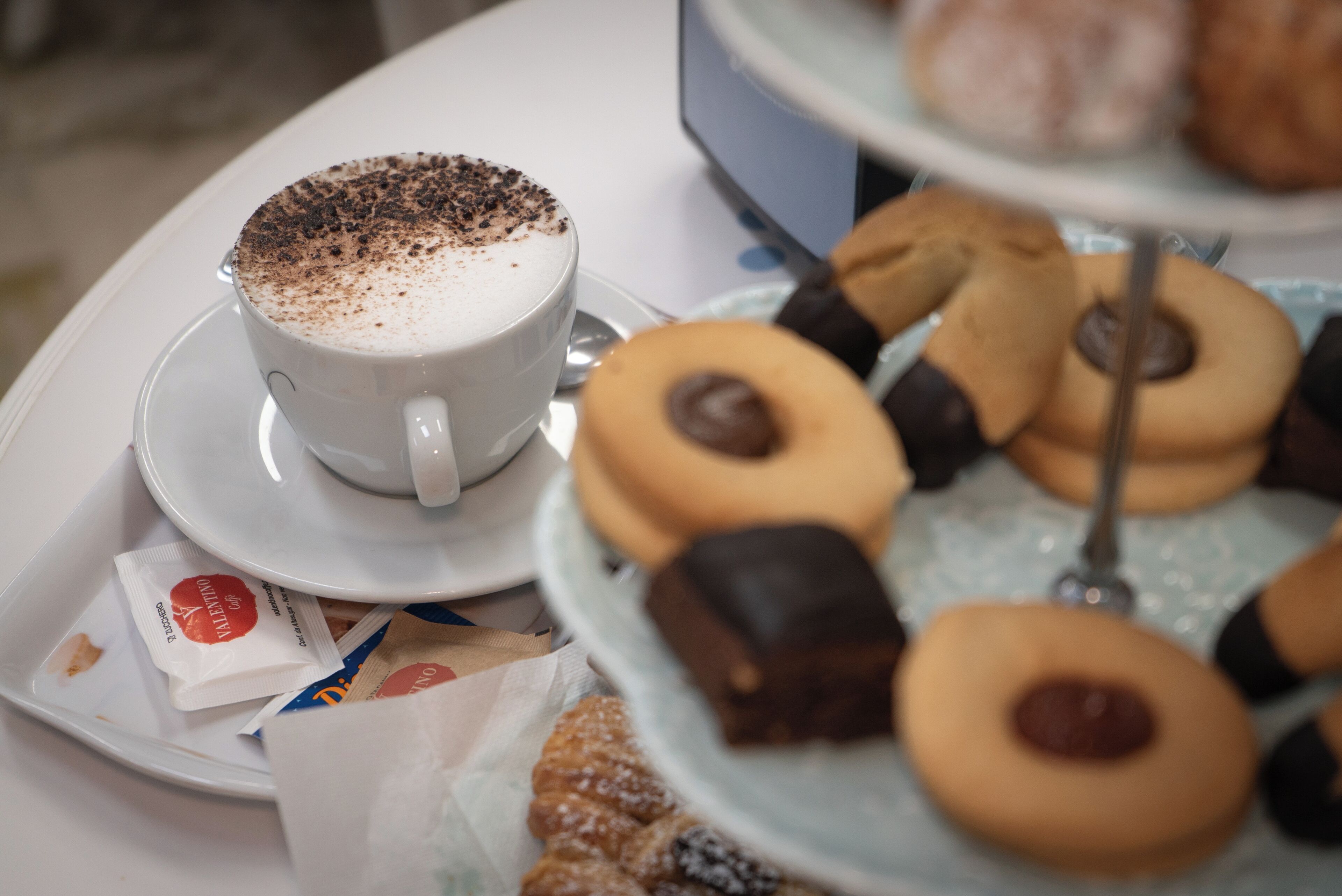 A table with a cup of coffee, a tray of pastries, and a plate of cookies.