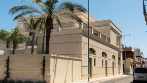 A multi-story building with a beige facade, a green door, and a palm tree in front. - BONA NOVA – Puglia Living (Massafra)