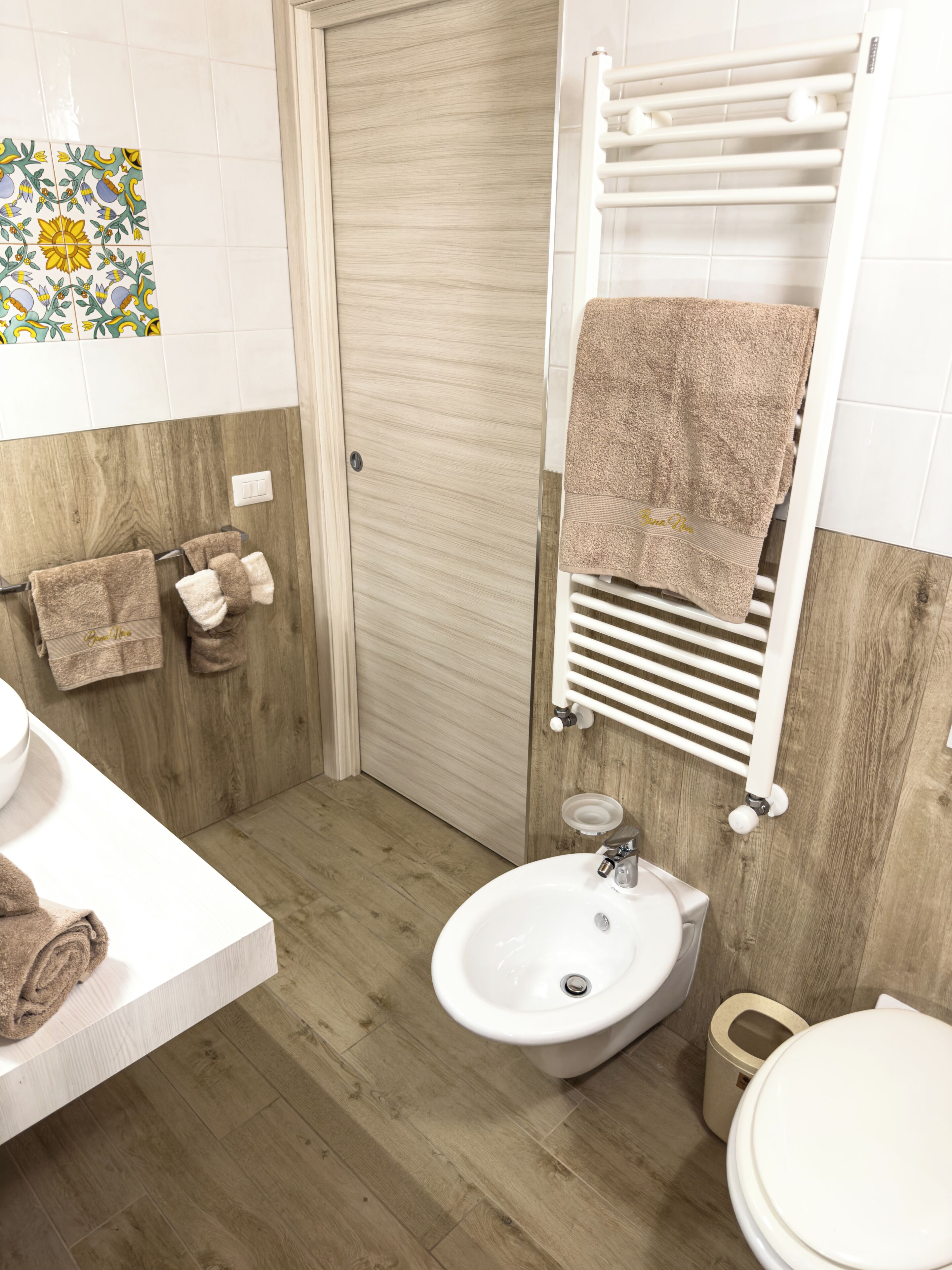 Ein Badezimmer mit Holzboden, einem weißen Waschbecken, einer Toilette und einem Handtuchhalter mit Handtüchern.