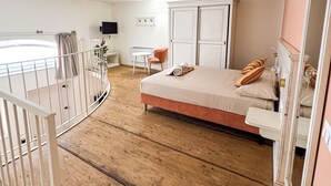A bedroom with a wooden floor, a bed with pillows, a chair, a TV, and a wardrobe. - BONA NOVA – Puglia Living (Massafra)