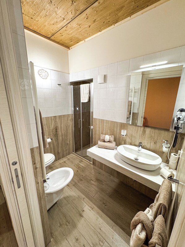 A modern bathroom with a wooden ceiling, a glass shower enclosure, a white sink, and a large mirror. - BONA NOVA – Puglia Living (Massafra)