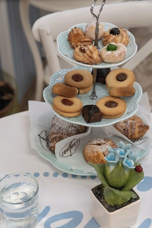 A tiered dessert stand with various pastries on a table with a small decorative plant and a glass of water.