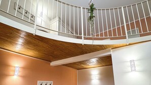 A spacious living area with a wooden ceiling, a white railing, a sofa, a dining table with chairs, and a potted plant. - BONA NOVA – Puglia Living (Massafra)