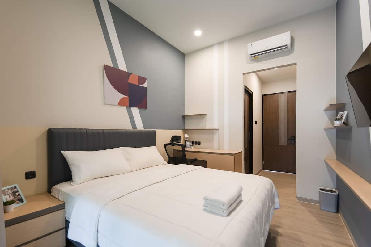 A modern hotel room with a large bed, a desk, a chair, and a TV.