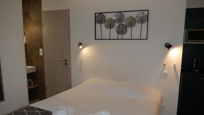 A neatly made bed with towels, a wall-mounted artwork, and a door leading to a bathroom. - Just 10 minutes from the town center, this cocooning studio is sure to make your stay a pleasant one! (Mulhouse)