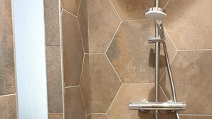 A shower area with hexagonal tiles and a chrome showerhead. - Just 10 minutes from the town center, this cocooning studio is sure to make your stay a pleasant one! (Mulhouse)