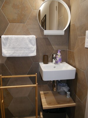 Un baño con un lavabo blanco, un espejo redondo, un perchero y un taburete de madera.