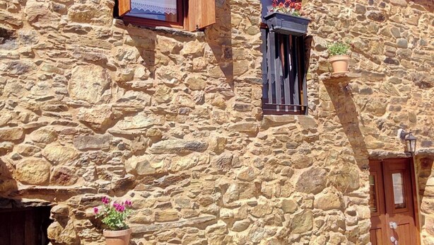 Ein Steinhaus mit Holztür und -fenstern, Blumentöpfen und einem Ziegeldach.