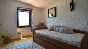 Ein Schlafzimmer mit einem hölzernen Bett, einem Fenster, einem Nachttisch, einer Lampe und einer Wandleuchte.
