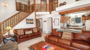 A spacious living area with a brown leather sofa, a wooden coffee table, and a staircase leading to an upper level. - Lemmon Lodge #30 – Lake Access with private sandy beach (Grand Lake)