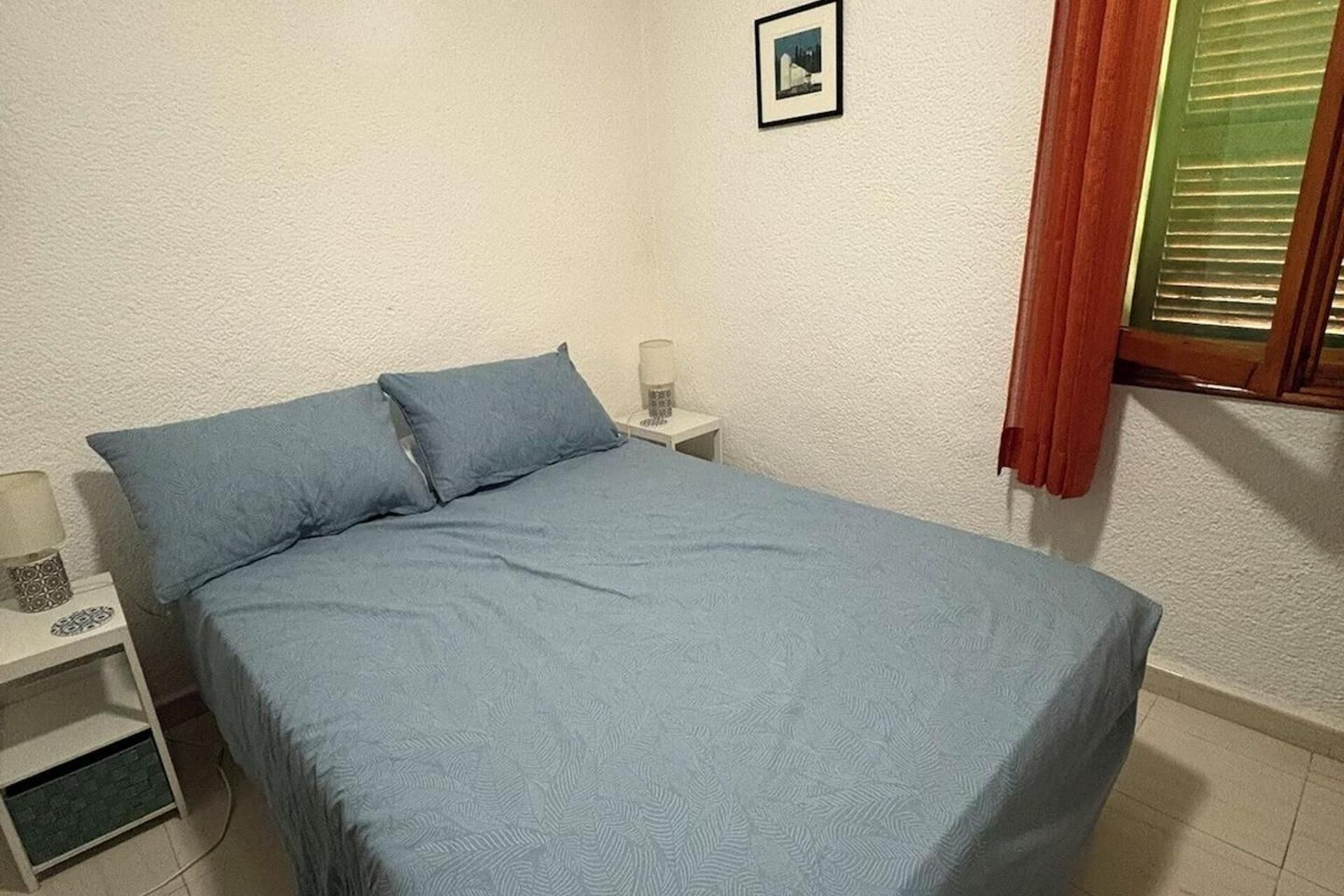 Un dormitorio con una cama, una mesita de noche, una lámpara y un cuadro en la pared.