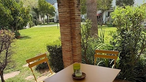 A patio with a table and two chairs, surrounded by lush greenery and a mountain in the background. - 1 Bed-sleeps 2-gardens-pool-10 Min To Beach (Denia)