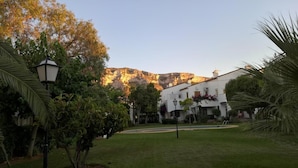 A courtyard with a white building, a mountain in the background, and a palm tree. - 1 Bed-sleeps 2-gardens-pool-10 Min To Beach (Denia)