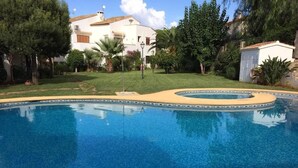 A swimming pool with a curved edge, surrounded by a grassy area and trees. - 1 Bed-sleeps 2-gardens-pool-10 Min To Beach (Denia)