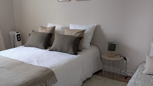 Une chambre à coucher bien rangée, avec un grand lit, une table de chevet avec une lampe et deux œuvres d’art encadrées accrochées au mur.