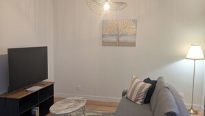 Un salon moderne avec un téléviseur à écran plat, un canapé gris, une table basse et un tableau accroché au mur.