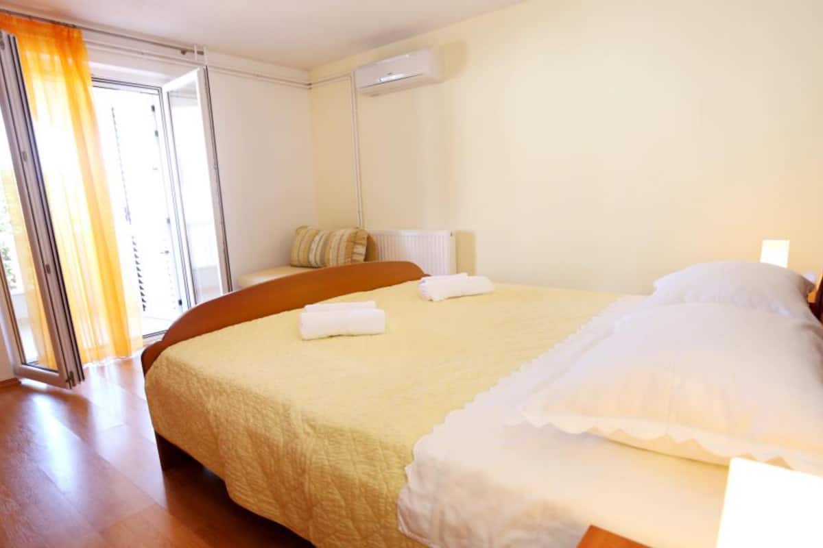 Une chambre d’hôtel avec un lit, une fenêtre avec des rideaux, un radiateur et un plancher en bois.