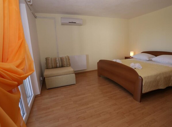 Une chambre avec un plancher en bois, un lit avec une literie blanche, une table de chevet avec une lampe et un radiateur.