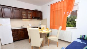 Cocina compacta con armarios de madera, una mesa de comedor con sillas y un ventanal con cortinas naranjas.