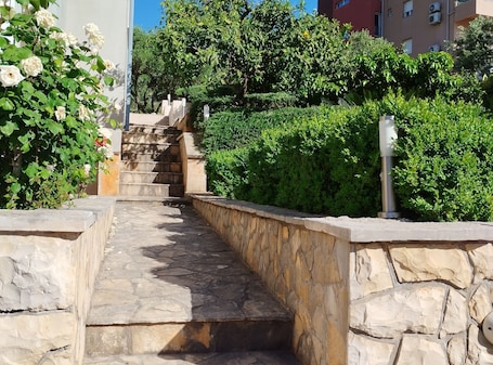 A stone staircase leading up to a building, surrounded by lush greenery and white flowers.